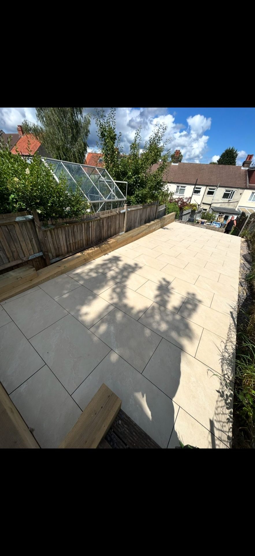 Large patio with raised planters and greenhouse by Burton Builds
